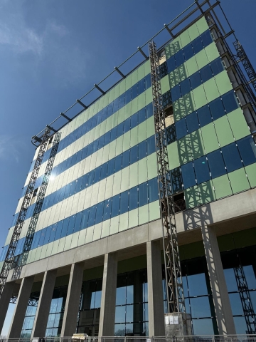 Vliesgevel in aluminium schrijnwerk van Lootens. Groen getint doorzichtglas afgewisseld met lichtgroene borsweringen. Dus afwisselend donkergroene en lichtgroene lijnen. Zomers gevoel.